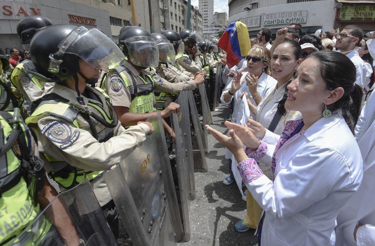 Doctors chant slogans in front of a line of National Guard personnel in riot gear during a demonstration against the shortage in medicines and in rejection of the government of President Nicolas Maduro, in Caracas on May , 17, 2017.
Venezuela's government said Wednesday it was sending troops to a western region rocked by looting and attacks against security installations during a wave of anti-government protests. / AFP PHOTO / JUAN BARRETO