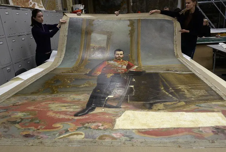 A picture taken in Saint Petersburg on November 17, 2016 shows restorers of the Stieglitz Art and Industry Academy displaying the portrait of Tsar Nicholas II by Ilya Galkin (1896) that was discovered beneath water-soluble paint on the back of the canvas used for the full-size portrait of Vladimir Lenin by Vladislav Izmailovich (1924).
A portrait of the last Tsar of Russia, Nicholas II, remained hidden for nearly a century under a portrait of Soviet state founder Vladimir Lenin, and discovered by chance will soon be exhibited in Saint Petersburg, according to restorers. / AFP PHOTO / Olga MALTSEVA