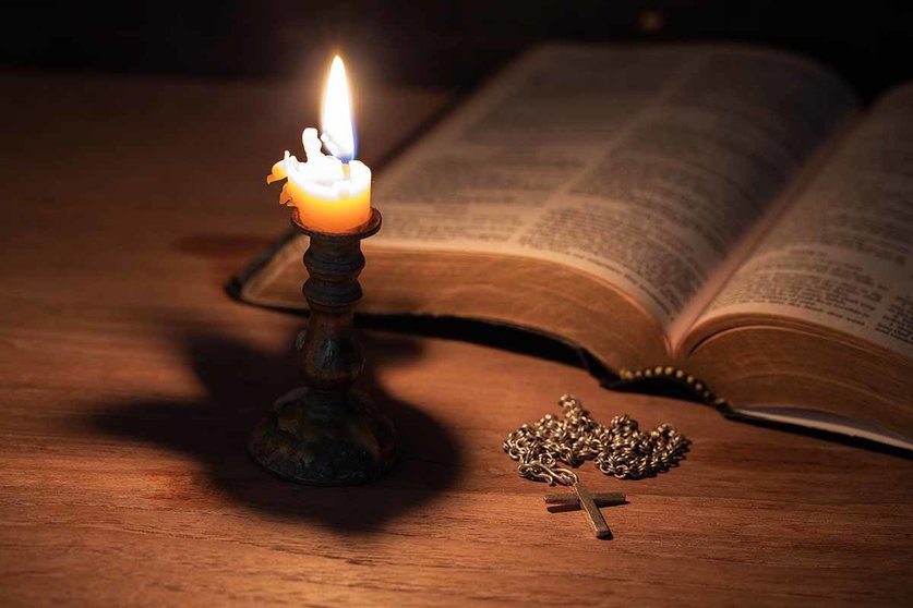 Bible, wood Cross and candles on an old wooden table with a dark background