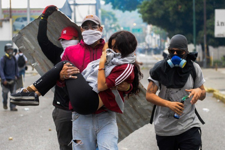 A young woman who was overcome by tear gas shot by tiot police is carried away by fellow demonstrators when opposition activists clashed with riot police in Caracas on April 10, 2017. 
Venezuela's political crisis intensified last week when the Supreme Court issued rulings curbing the powers of the opposition-controlled legislature. The court reversed the rulings days later, but the opposition intensified its protests from that moment.
 / AFP PHOTO / FEDERICO PARRA