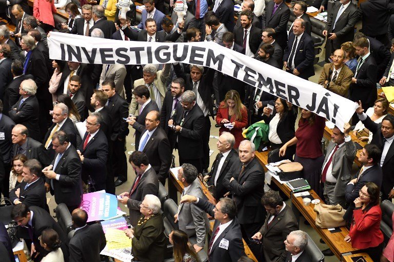 Opposition lawmakers hold a banner reading 'Investigate Temer now!' referring to Brazilian President Michel Temer at the House of Representatives in Brasilia, on August 2, 2017. 
Brazilian lawmakers angrily debated Wednesday ahead of an unprecedented vote on whether President Michel Temer should face trial for alleged corruption, just a year after his predecessor was booted from office. / AFP PHOTO / EVARISTO SA