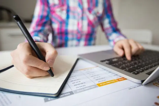 persona-de-negocios-trabajando-en-la-computadora-portatil-y-haciendo-notas_1262-3150