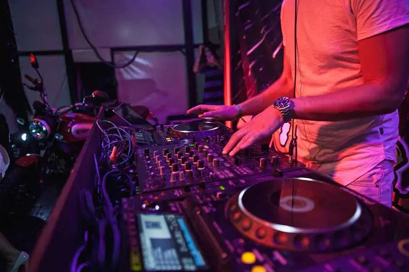 DJ playing music at mixer on colorful blurred background. The hands close up