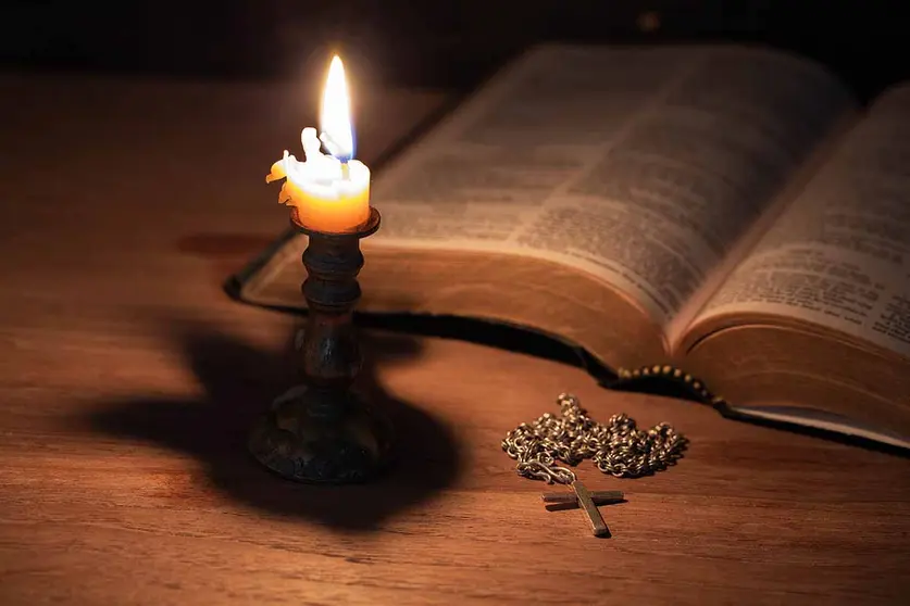 Bible, wood Cross and candles on an old wooden table with a dark background