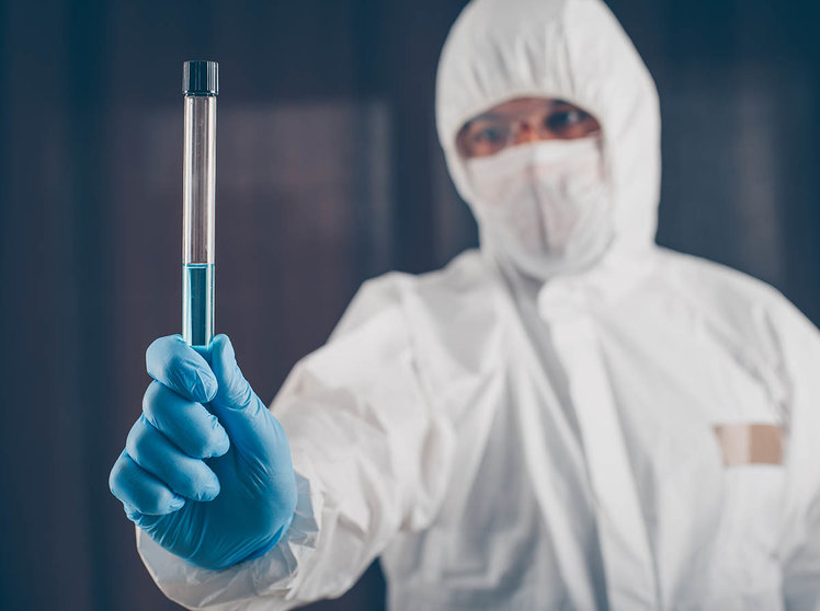 A doctor holding long glass vial medicine cure in dark background in mask, gloves and protective suit . coronavirus.