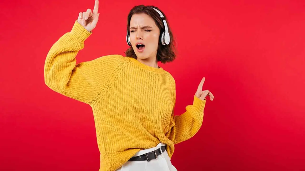 Portrait of a cheerful woman in headphones listening to music and dancing isolated over pink background