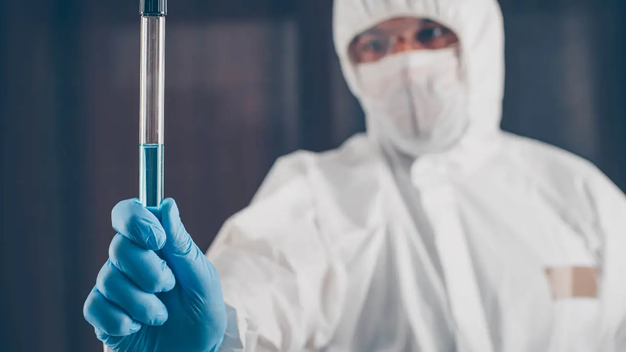 A doctor holding long glass vial medicine cure in dark background in mask, gloves and protective suit . coronavirus.