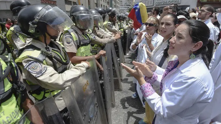 Doctors chant slogans in front of a line of National Guard personnel in riot gear during a demonstration against the shortage in medicines and in rejection of the government of President Nicolas Maduro, in Caracas on May , 17, 2017.
Venezuela's government said Wednesday it was sending troops to a western region rocked by looting and attacks against security installations during a wave of anti-government protests. / AFP PHOTO / JUAN BARRETO