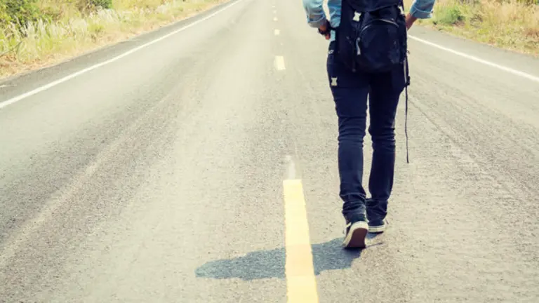 Rear view of a young woman hitchhiking carrying backpack walking on the road
