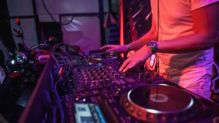 DJ playing music at mixer on colorful blurred background. The hands close up