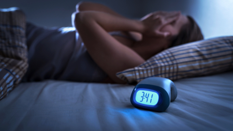 Sleepless woman suffering from insomnia, sleep apnea or stress. Tired and exhausted lady. Headache or migraine. Awake in the middle of the night. Frustrated person with problem. Alarm clock with time.